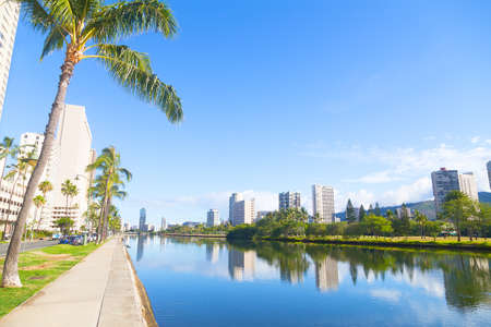 The picturesque panorama of Waikiki suburbs along the canal with reflections, Honolulu, Hawaii, USA. A promenade near the canal with palm trees.の写真素材
