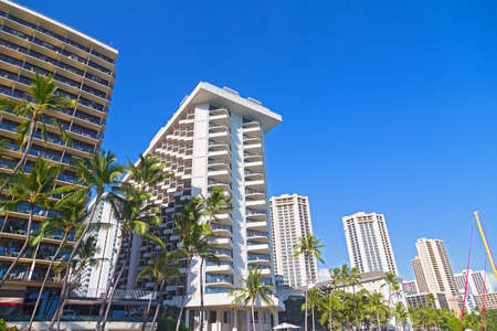 Waikiki beach waterfront buildings under tropical blue sky, Hawaii, USA. Modern buildings on a street with tall palm trees.の写真素材