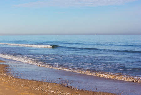 Costa Blanca sandy beach in winter, Valencia region, Spain. Gentle waves bring shells on the beach.の写真素材
