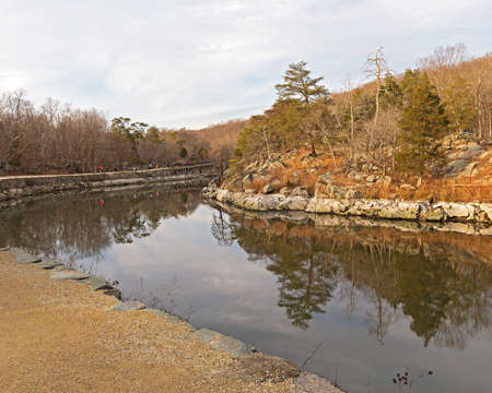 Scenic winter landscape along the canal with footpath and rocky banks. Forest landscape with trees reflection in canal waters.の写真素材