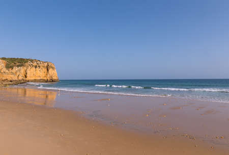 Atlantic beach at sunset during low tide. Waves are rolling on a sandy beach in Algarve, Portugal.の写真素材