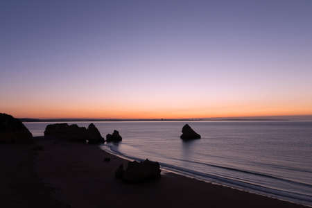Sunrise over the ocean in Lagos, Portugal. Empty sandy beach with rock formations at sunrise.の写真素材