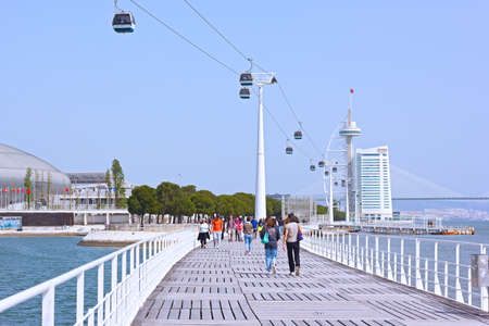 LISBON, PORTUGAL â APRIL 25, 2018: People taking a stroll along Tagus River in unusually warm spring morning with cable cabins, Myriad Hotel and the tower on background.のeditorial素材