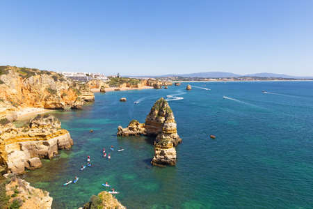 Scenic cliffs and grottos explore by tourists by kayaks and boats in Algarve, Portugal. Scenic coastline with sandy beaches and water sport activities in the morning.の写真素材