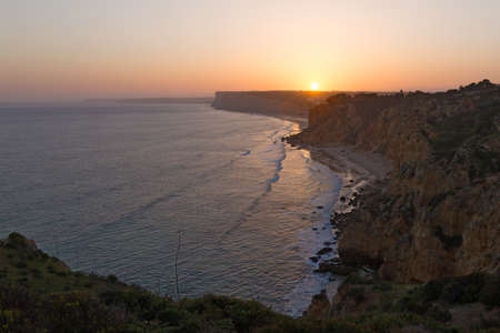 Sunset over a coastline of the Atlantic Ocean. Sun disk goes down behind the cliffs in Lagos, Portugal.の写真素材