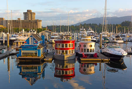 VANCOUVER, CANADA â JULY 1, 2017: Boat houses on the water of Coal Harbour Marina at sunrise. City panorama with floating boathouses, forest, and mountain ridges on the horizon.のeditorial素材