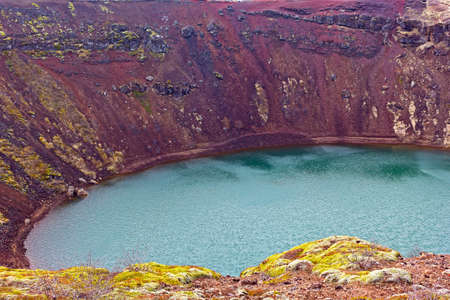 Distinctive red rock and vegetation on one edge of a volcanic crater lake in south Iceland. A beauty of easy recognizable volcanic crater lake in Iceland, Europe.の写真素材