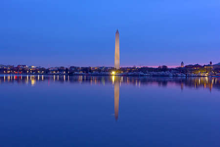 US capital panorama along Tidal Basin reservoir during cherry blossom at dawn. Easy recognizable Washington Monument with reflection in water stands tall on horizon.の写真素材
