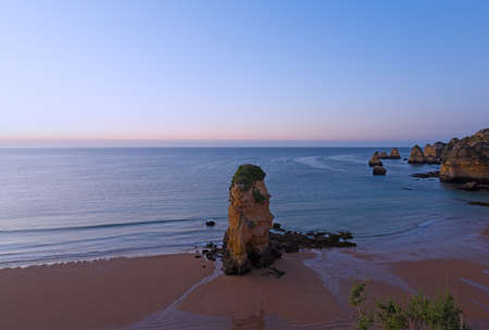Empty sandy beach with whimsy cliffs at sunrise in Lagos, Portugal. Cloudy sunrise over the Atlantic Ocean.の写真素材