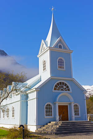Scenic wooden church painted in blue color against mountainous landscape in Northern Iceland. Icelandic traditional official building structure with framed windows and decorative bits of adornment.の写真素材