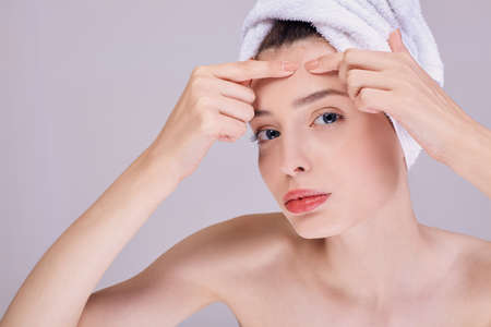 Young beautiful girl after a shower, half-naked, in a white towel on her head crushes acne on her face. Imperfections in the skin. Beauty procedures. The concept of beauty and care.の写真素材