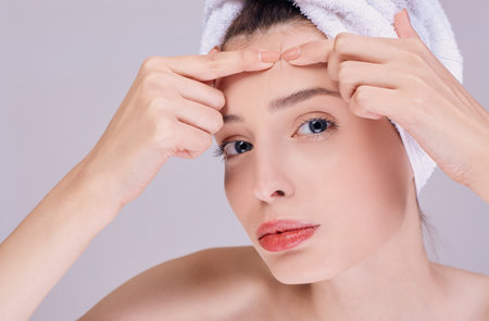 Young beautiful girl after a shower, half-naked, in a white towel on her head crushes acne on her...