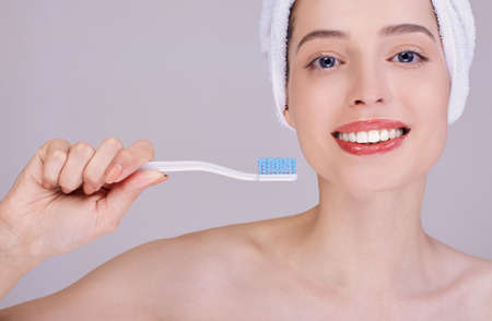 A young woman in a towel after a shower, holds a toothbrush, has a morning routine, shows bare shoulders, healthy skin. Dental care and dental health. Close-up.の写真素材