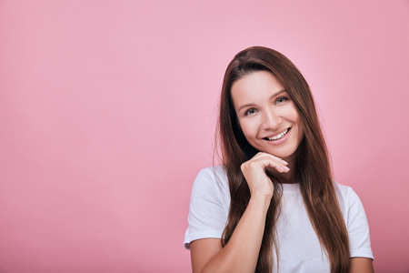 Cute cool attractive girl with brown hair standing on a pink wall back. Life style, emotions. The woman put her hand under her head and smiles sweetly.の写真素材