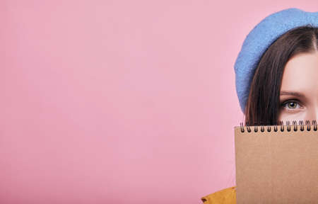 Cool teenager with dark hair in blue barret and yellow raincoat is standing with a brown notebook. Lady looking right with one eye in the frame.の写真素材