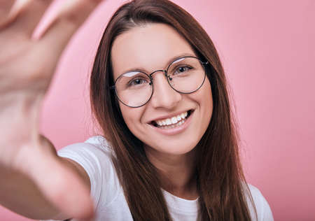 Cute charming cool happy smiling girl in glasses in a white T-shirt holds a camera with her hand and takes a selfie. Lifestyle, photographs, emotional.の写真素材