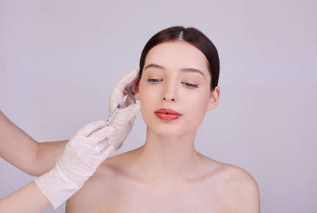 A cosmetologist makes anti-aging procedures for face injections to tighten and smooth wrinkles on the face skin of a beautiful, young woman in a beauty salon. Cosmetology skin care.の写真素材