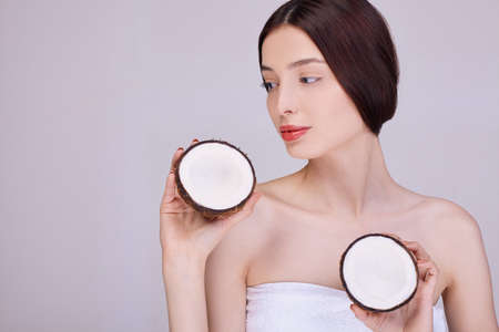 Beautiful young girl with a light natural make-up and perfect skin with a coconut in her hand. Beauty face. Photo taken in the studio on the background.の写真素材