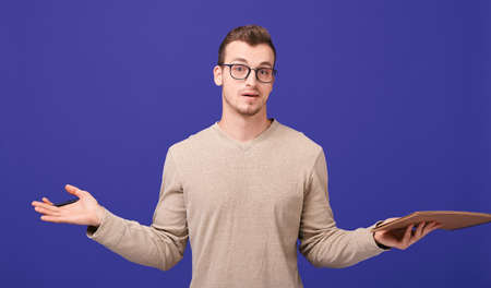 Pensive author of book with draft notebook and ballpoint pen, doubts himself. A boy in beige sweater and glasses spread his arms to the side. Copy spaceの写真素材