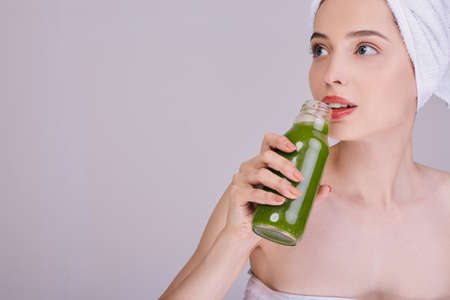 Lady after a shower enjoys a green smoothie in a bottle. A beautiful girl with blue eyes. Healthy eating, Keto diet. Detox. Body cleansing.の写真素材