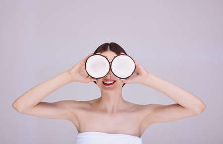 Beautiful young girl with long eyelashes and perfect skin make-up with coconuts in hands in the studio on a white background. Beauty face, hair care. Coconut glasses.の写真素材