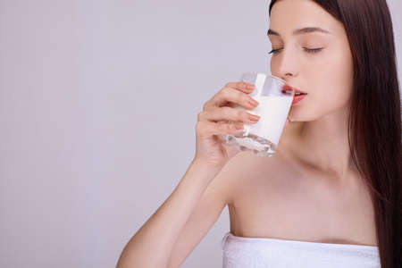 A young girl with well-groomed skin and dark hair, closing her eyes, drinks milk from a glass. Proper nutrition. Lactic acid, lactose. Healthy teeth. Calcium Vegetable Milk.の写真素材