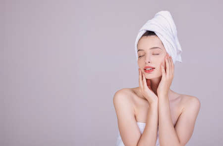 Image of adorable half-naked woman wrapped in a towel, smiling after a shower with hands on her face. Sensuality and tenderness. Care and care. Beauty concept. Natural beauty.の写真素材