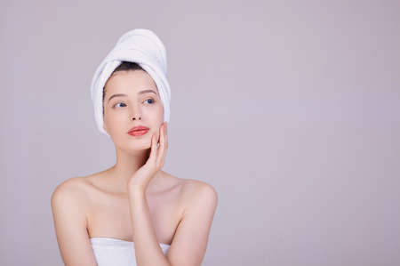 Woman with dark hair, with a towel on her head, after a shower, touches her face with her left hand. Sensuality and tenderness. Beauty concept. Face and body care.の写真素材