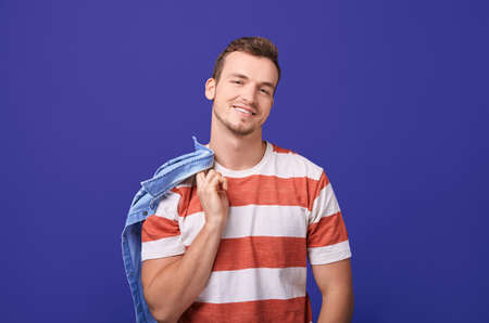 Confident teenager in a red and white striped t-shirt stands in the background and smiles. In one arm behind a guy holds a denim shirt. Close up, copy space.の写真素材