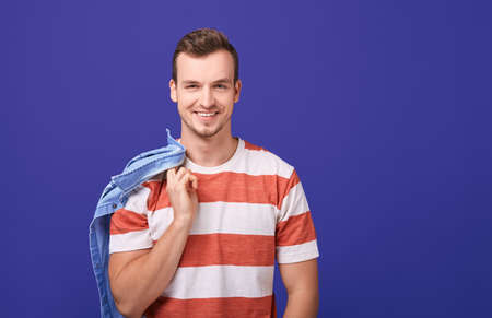 Confident beauty teenager in a red and white striped t-shirt stands in the background, smiles and looks straight. In one arm behind a guy holds a denim shirt. Close up, copy space.の写真素材