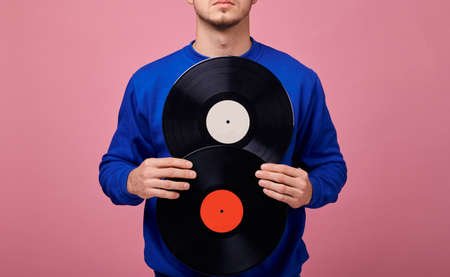 A hands of guy in dark blue jacket holds two black vinyl records in pink background. Retro style. Copy space. Close-up.の写真素材
