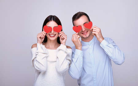 Cheerful young couple holding red paper hearts in their hands and smiling. Young lovers on Valentine's Day. Give valentines to each other. Photo on a light background.の写真素材