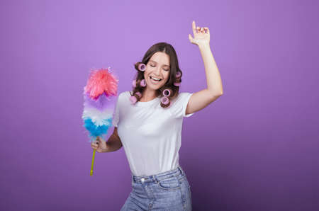 Beautiful girl in curlers and a white T-shirt sings songs and dances while cleaning. Housewife. Cleang. Maid. Cleanliness and cleaning. Homemade routine. House cleaning.の写真素材
