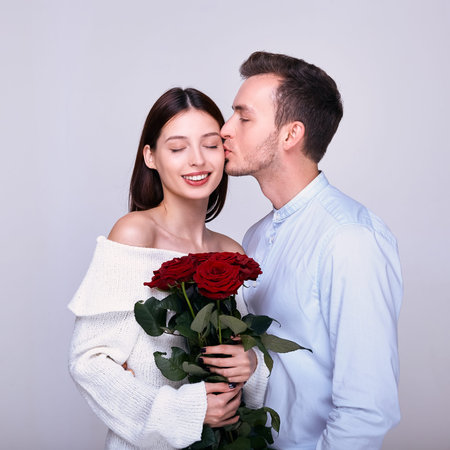 Tender beautiful brown-haired woman with full lips and a smile, holds red roses, covered her eyes...