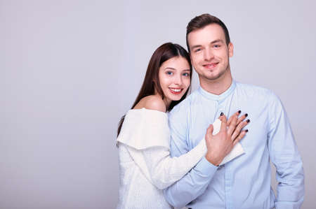 Happy and loving young couple posing. The brown-eyed girl put her hand on the guy's chest. The young guy smiles happily, holds the hand of his beloved. Festive atmosphere.の写真素材