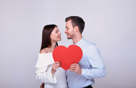 Romantic couple holding a big paper red heart in their hands and looking at each other. Young brown-haired woman in love looks at the guy. Valentine's Day. Love and family. The 14th of February.の写真素材