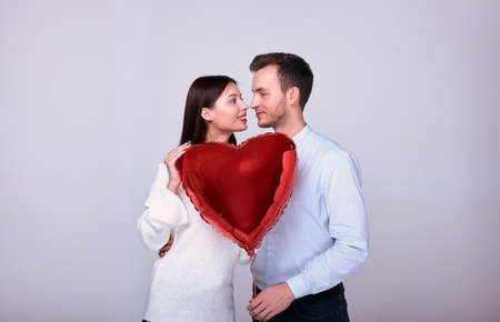 Cute young couple gently look at each other and smile. Lovers hold in bunches a balloon in the shape of a big red heart. Valentine's Day. An emotion of calm and joy. Photo on the background.の写真素材