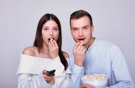 A young couple watching TV, movies, TV shows and enthusiastically eat popcorn. Family weekend. Time together. Family and entertainment concept.の写真素材