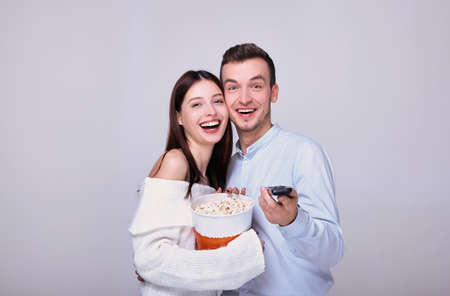 A happy couple of young guys have fun eating popcorn and watching movies. Weekend at home. Joint pastime. Love and family. People in love. Valentine's Day. Photo on a gray background.の写真素材