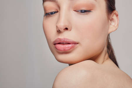 Young beautiful tender pritty girl with blue eyes and full lips. Grey background. Dark hair. Looking down. Copy space. Spa, cosmetology.の写真素材