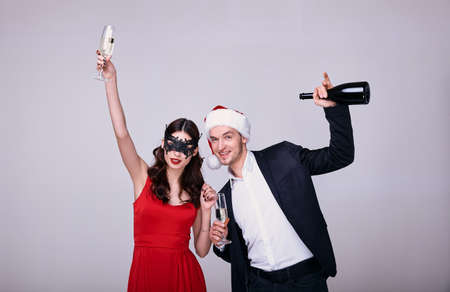 Elegant couple in stylish clothes having fun on a white background. New Year's carnival party. Young stylish couple in love on white background holding glasses and drinking champagneの写真素材