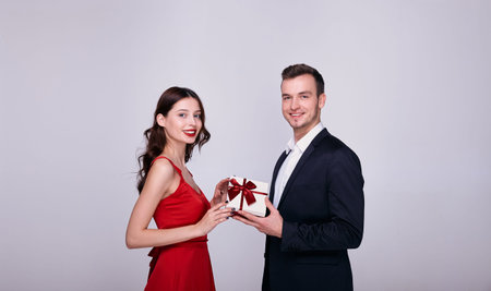 Handsome young man with a smile gives a gift to a girl in a red dress. New Year surprise, Christmas...