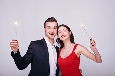 Happy, young beautiful couple on New Year's Eve holds sparklers in their hands. A girl in a red...