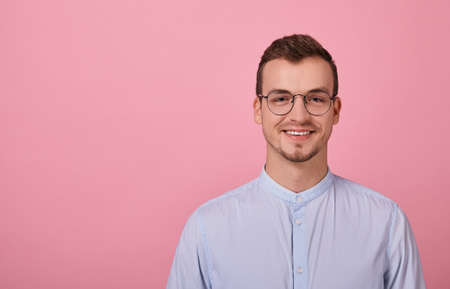 A decent young man in a sky blue shirt and computer glasses stands on a pink background. Student, businessman, employee of the year. Happy.の写真素材