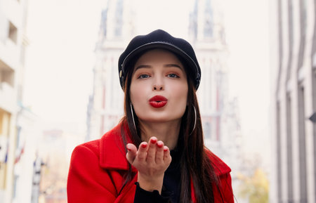 A stunning charming unsurpassed girl with bright red lips and brown hair in a cool red coat and a...