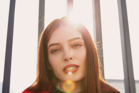 Inviting sweet cute girl with nice blue eyes clings to both bars and hangs on it, and looks seductively into the frame. The sun hangs overhead and falls into the frame.の写真素材