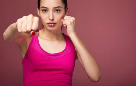 A white girl in a pink top folded her hands in fists and extended her hand forward. Girl boxing on a pink background. The girl is engaged in boxing, self-defense, strong in mind and body. Copy space.の写真素材