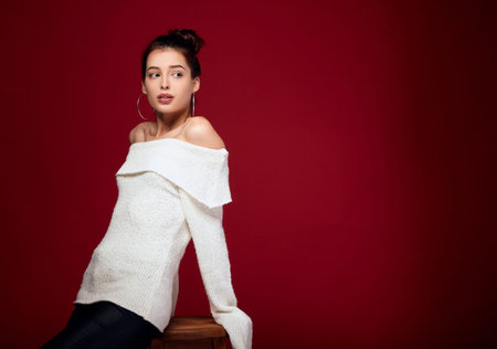 A delightful charming fashionable girl with pure radiant white skin, blue eyes, looks to the side. Fashion model poses on a red background in warm clothes. Beautiful young woman dreams. Copy space.の写真素材