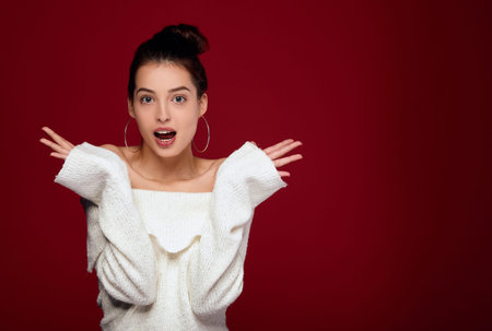 Attractive pretty white girl with dark hair and blue eyes in a white knitted sweater raised her...