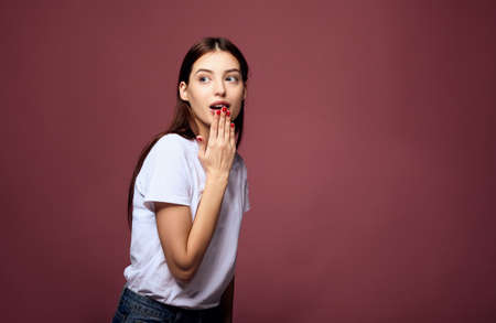 Surprised beautiful young Caucasian woman in a white T-shirt in blue jeans with red manicure heard the important news, a secret, overhears posing on a pink background. Copy space.の写真素材